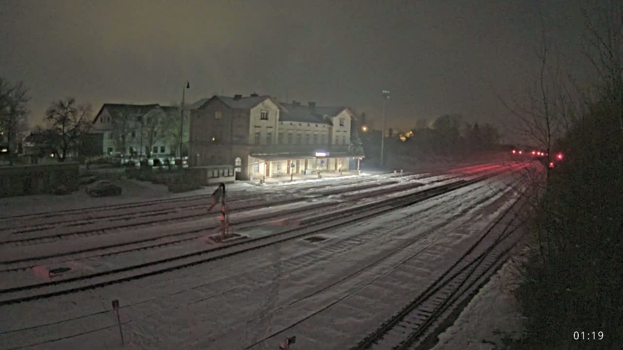 A snow-covered train station and tracks are illuminated at night.