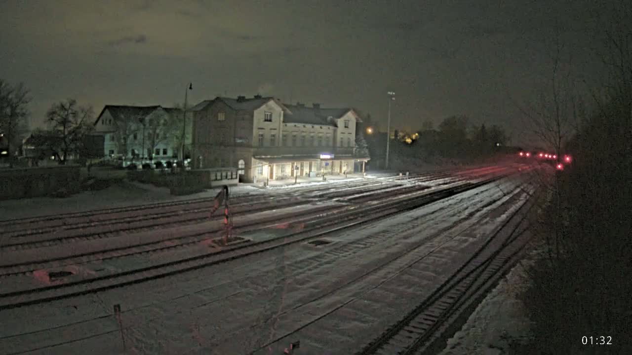 A snow-covered train station at night, with a long stretch of tracks extending into the darkness.