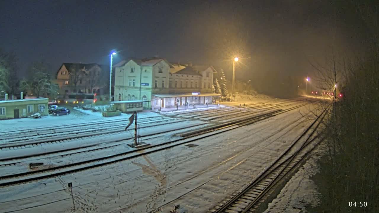 A snow-covered train station at night, illuminated by streetlights, with several train tracks extending into the distance.