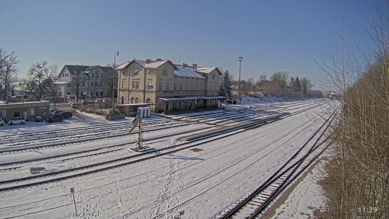 A snow-covered train station with several tracks extending into the distance under a clear, sunny sky.