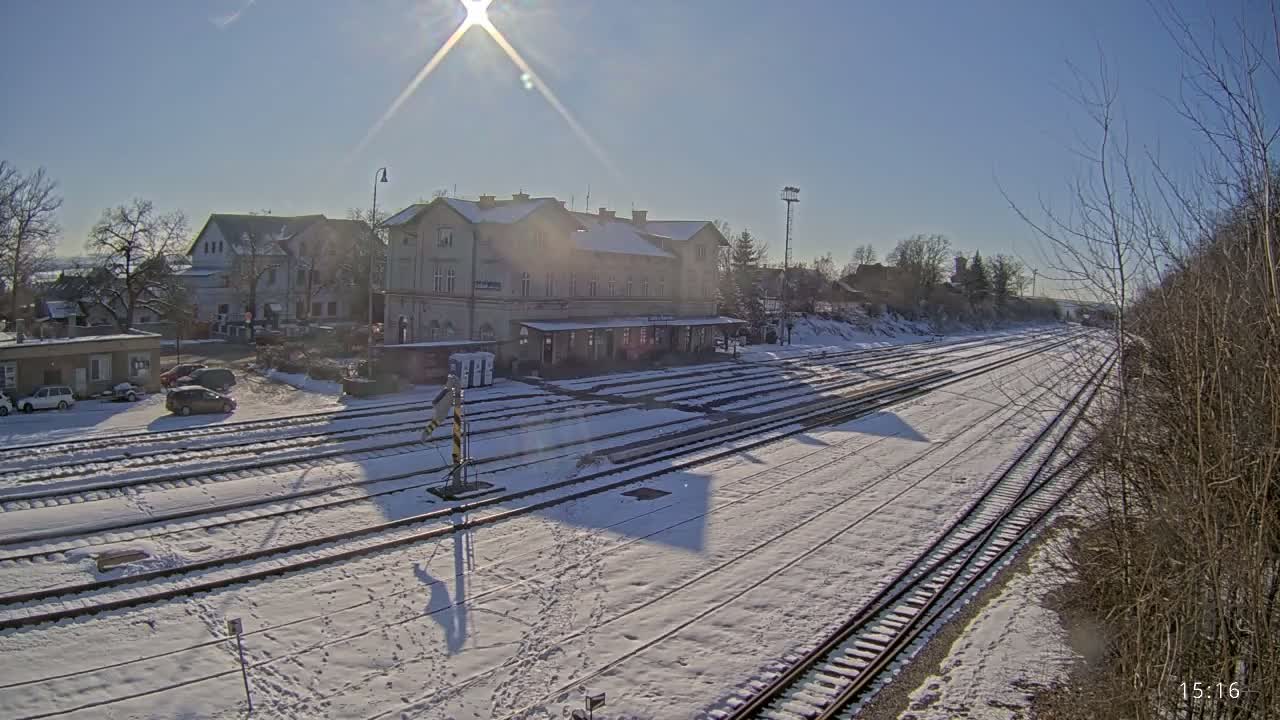 A snow-covered train station and tracks are seen on a sunny winter day.