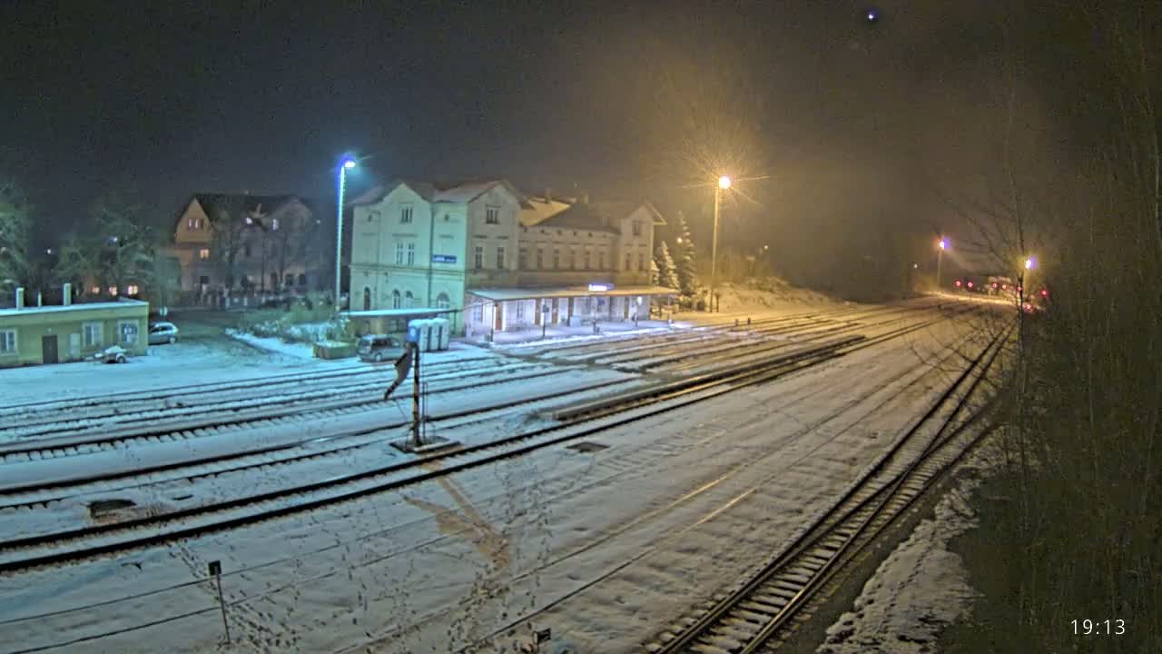 A snow-covered train station at night, illuminated by streetlights, with several sets of train tracks extending into the distance.