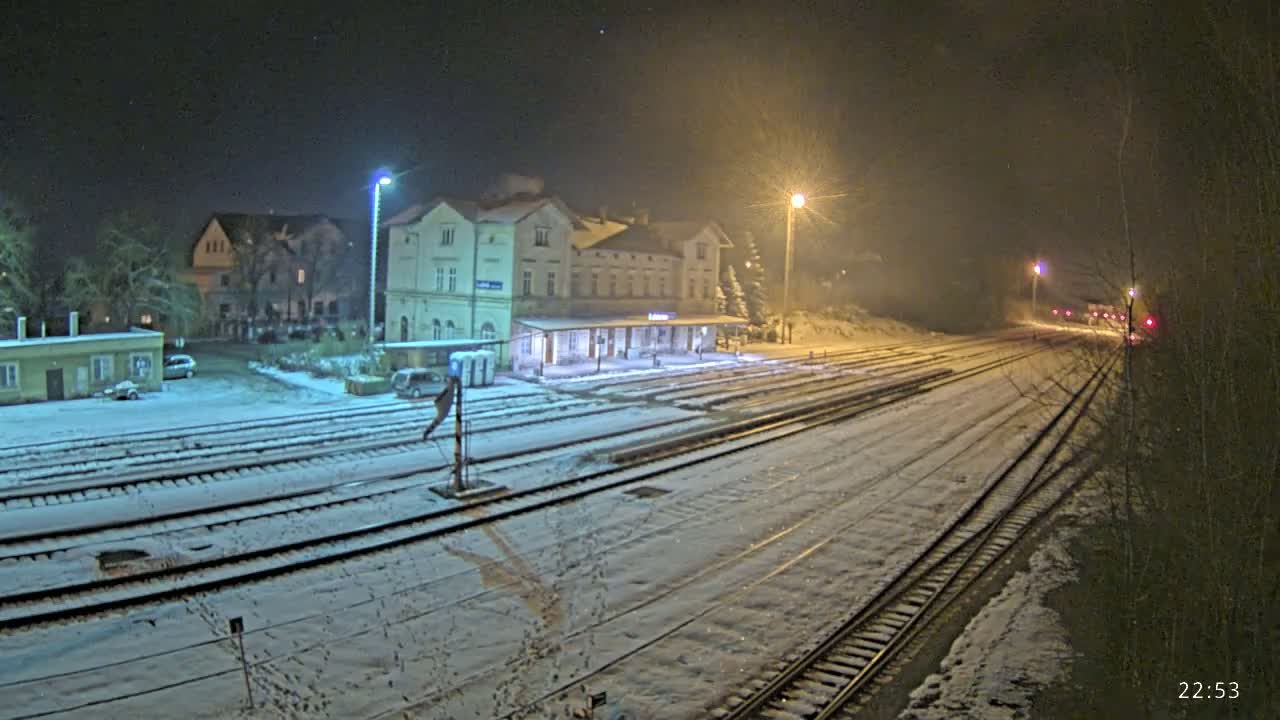 A snow-covered train station and tracks are illuminated at night by streetlights.