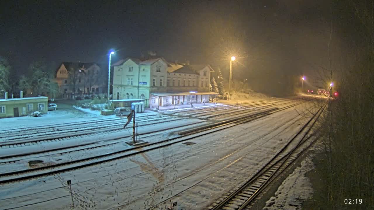 A snow-covered train station at night, illuminated by streetlights, with several tracks extending into the distance.