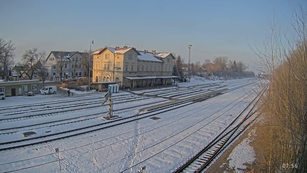 A snow-covered train station with multiple tracks extends into the distance on a clear, sunny day.