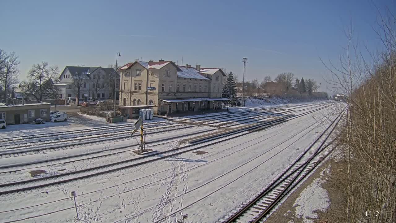 A snow-covered train station with several tracks extending into the distance under a clear blue sky.
