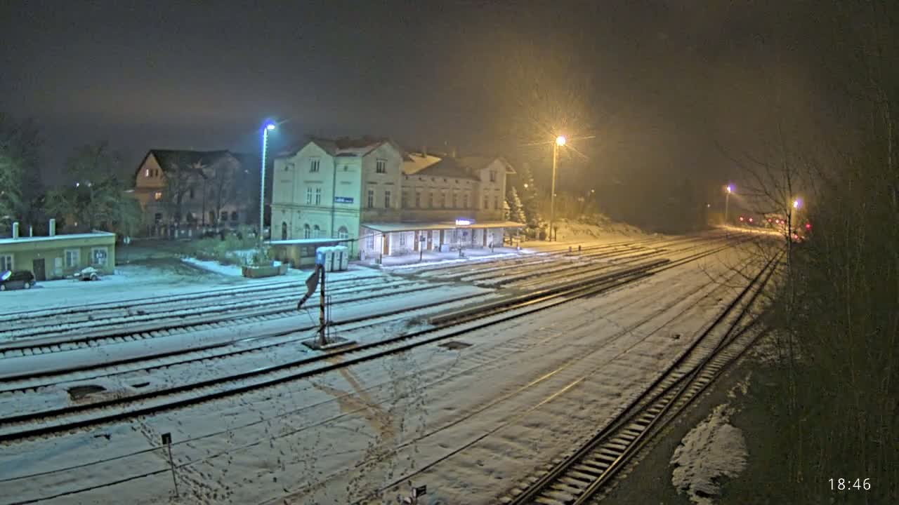 A snow-covered train station at night, illuminated by streetlights, with multiple train tracks extending into the distance.