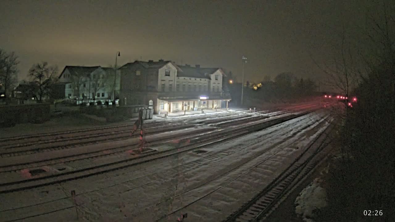 A snow-covered train station and tracks are illuminated at night.