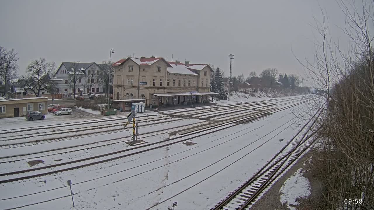 A snow-covered train station with multiple tracks extends into the distance under a gray sky.