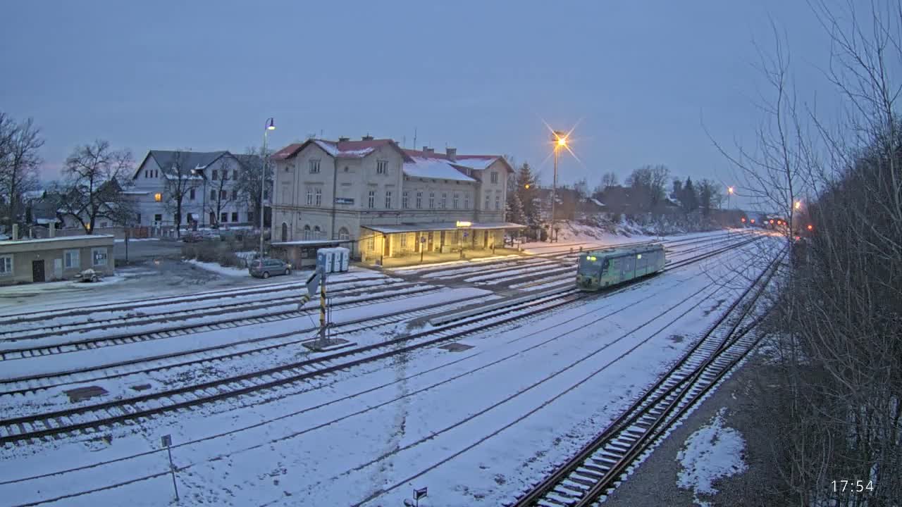 A train is arriving at a snow-covered train station in the early evening.