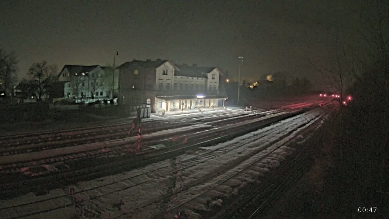 A snow-covered train station and tracks are illuminated at night.