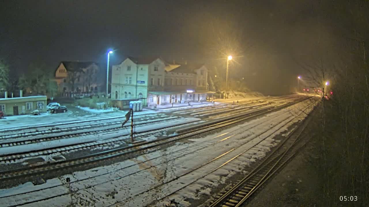 A snow-covered train station at night, illuminated by several streetlights.