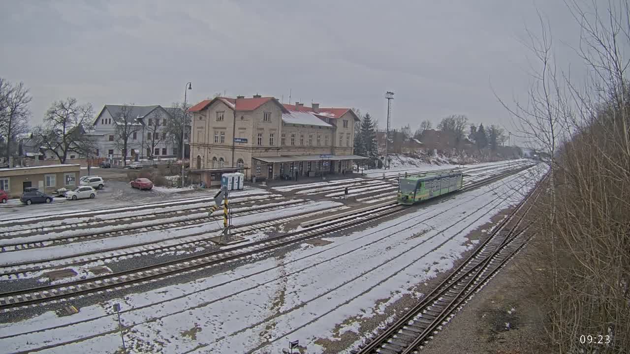 A light-green train is arriving at a snow-covered train station on an overcast day.
