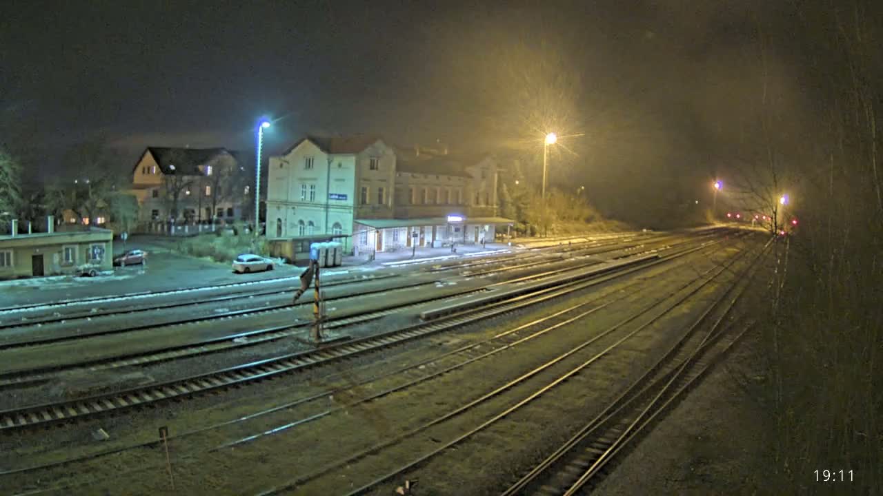 A nighttime view of a train station with several tracks extending into the distance under hazy, dimly lit conditions.