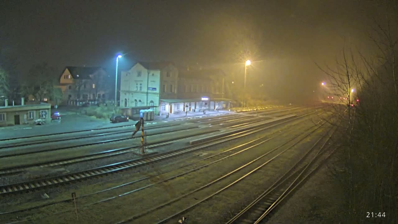A mostly empty train station at night in foggy conditions, with several sets of train tracks extending into the distance.