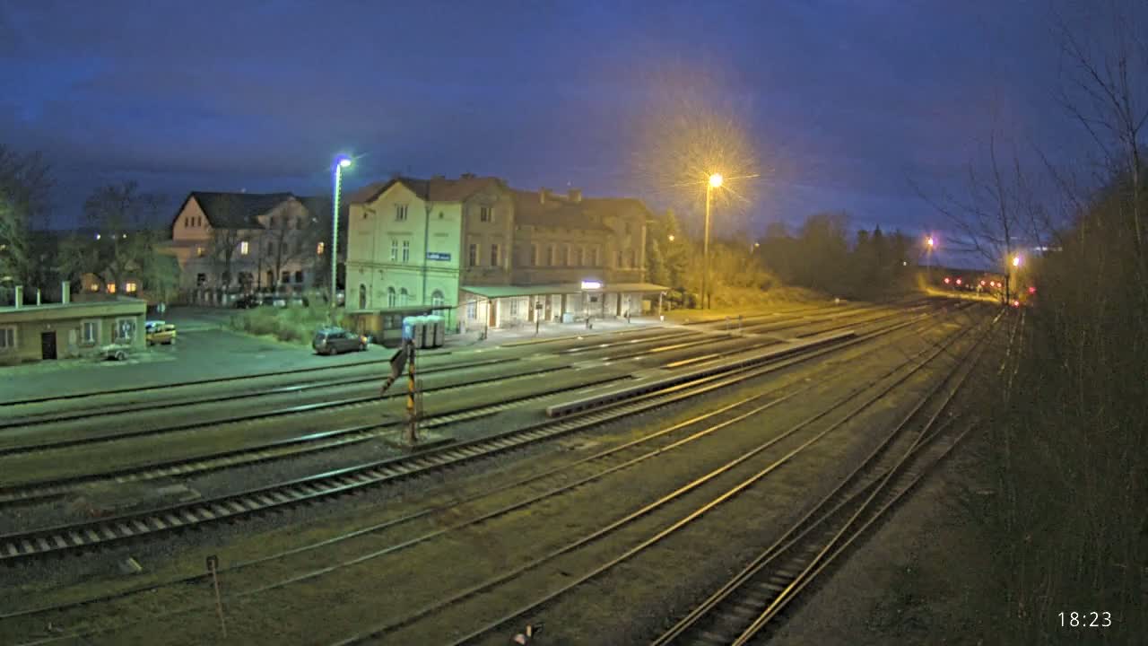A train station at night, under a twilight sky, with several sets of train tracks extending into the distance.