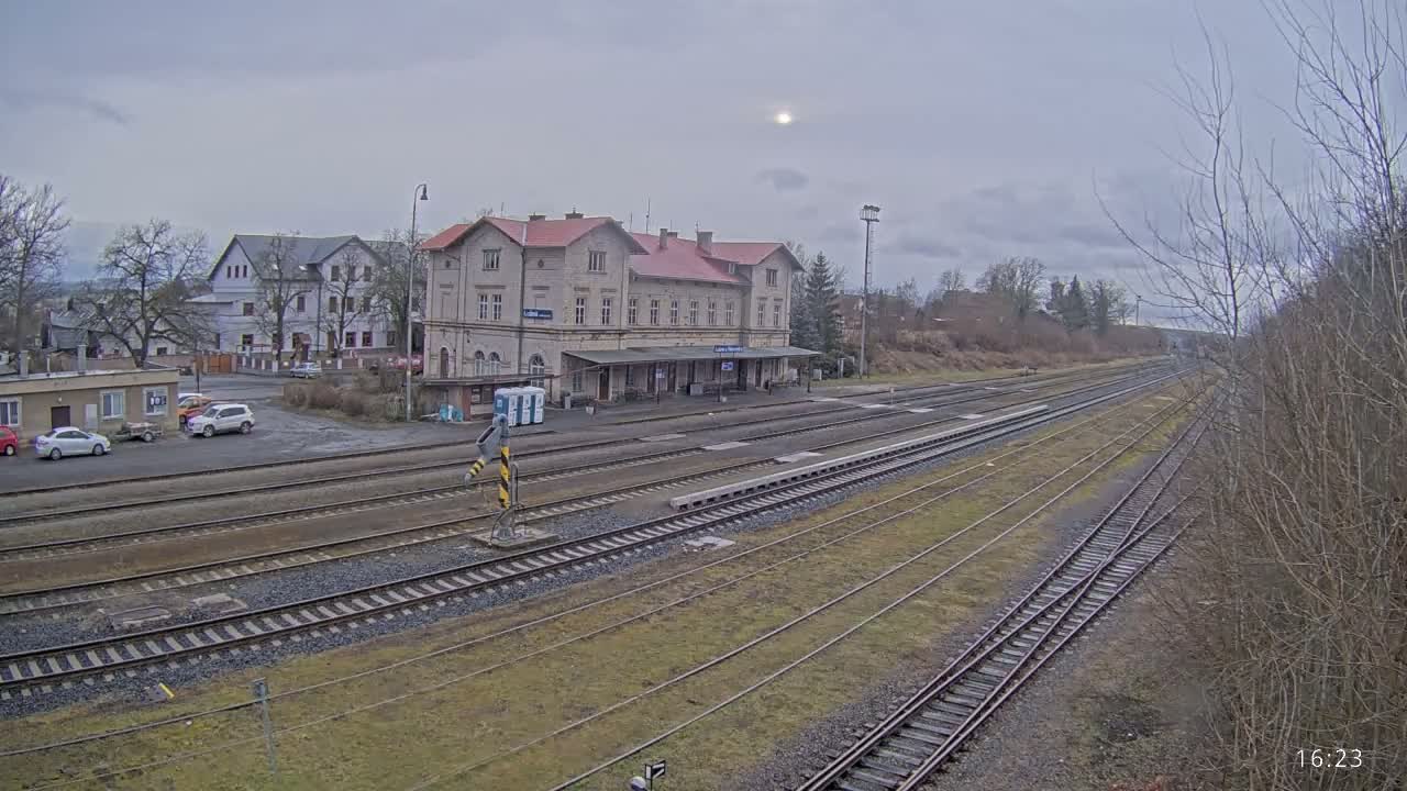 A train station with a long platform and several train tracks stretches out under an overcast sky.