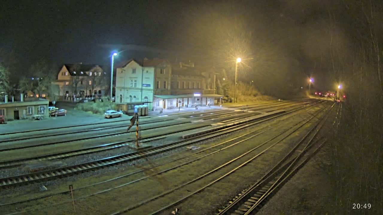 A nighttime view of a train station with several tracks extending into the distance under partly cloudy skies.
