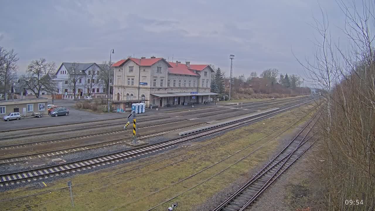 A train station with a long platform and several tracks is seen on an overcast day.