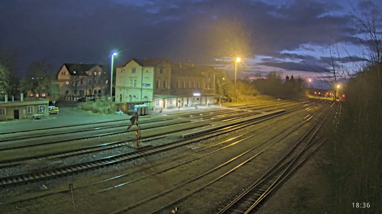 A nighttime view of a train station with several tracks extending into the distance under a partly cloudy sky.