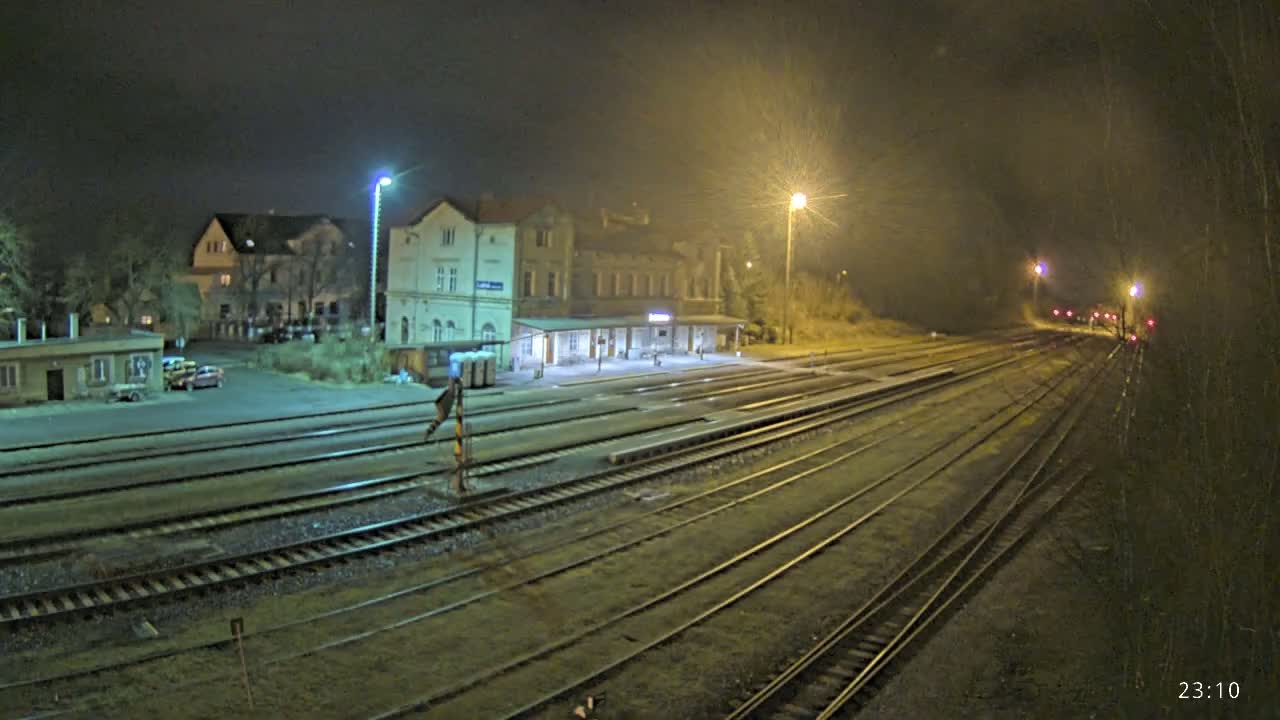 A nighttime view of a train station with multiple tracks extending into the distance under hazy, dimly lit conditions.