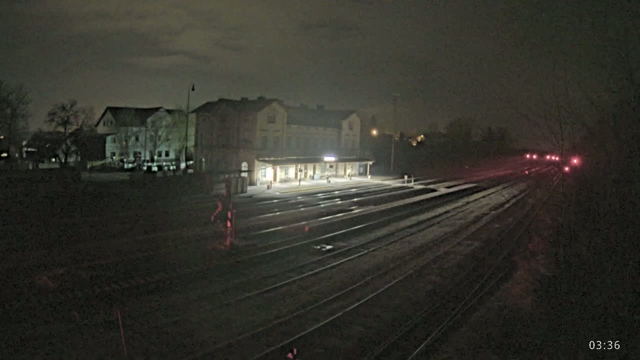 A dimly lit train station at night with several sets of train tracks extending into the darkness, under a cloudy sky.