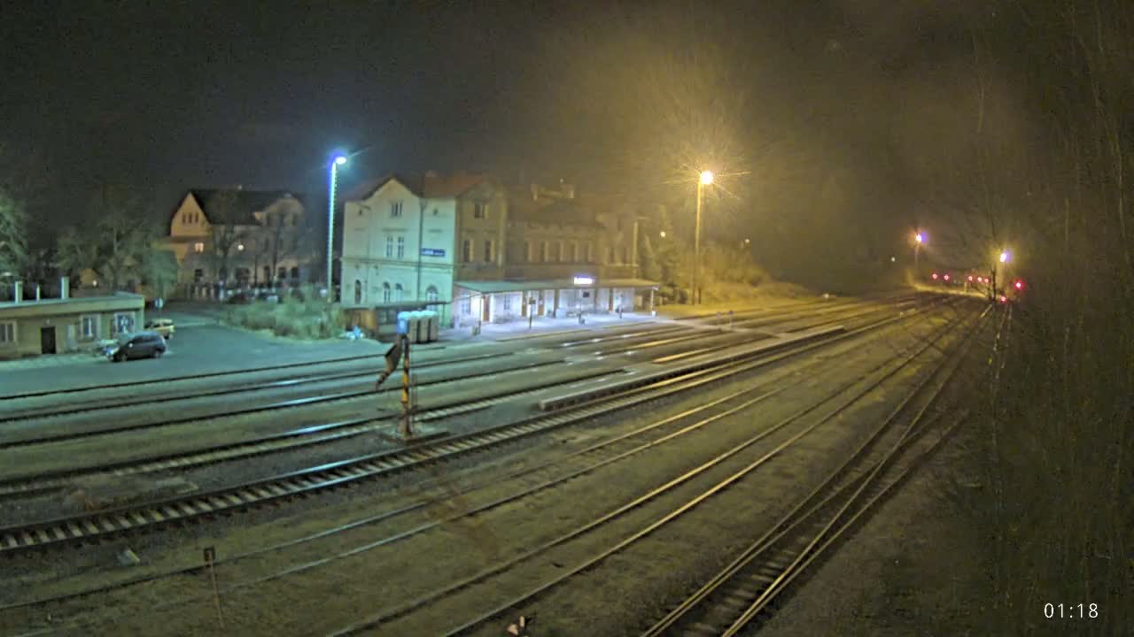 A nighttime view of a train station with several tracks extending into the distance under hazy, dimly lit conditions.