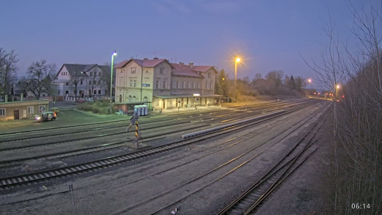 A long train track stretches away from a train station building under a twilight sky.