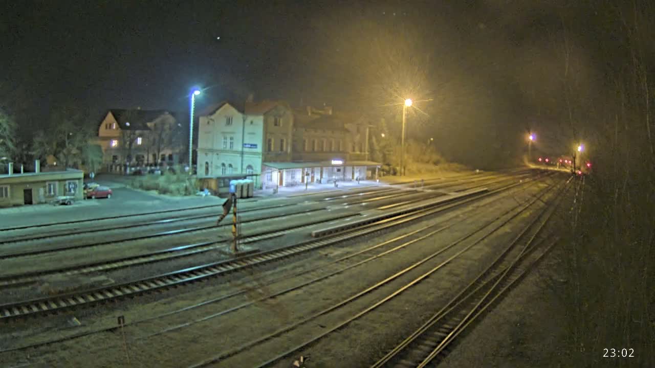 A nighttime view of a train station with multiple tracks extending into the distance under hazy, illuminated conditions.