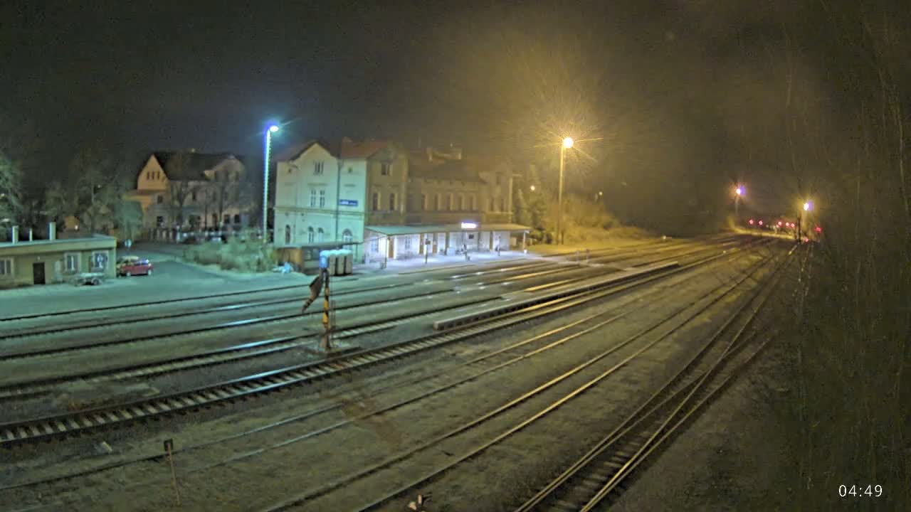 A nighttime view of a train station with multiple tracks extending into the distance under hazy, dimly lit conditions.