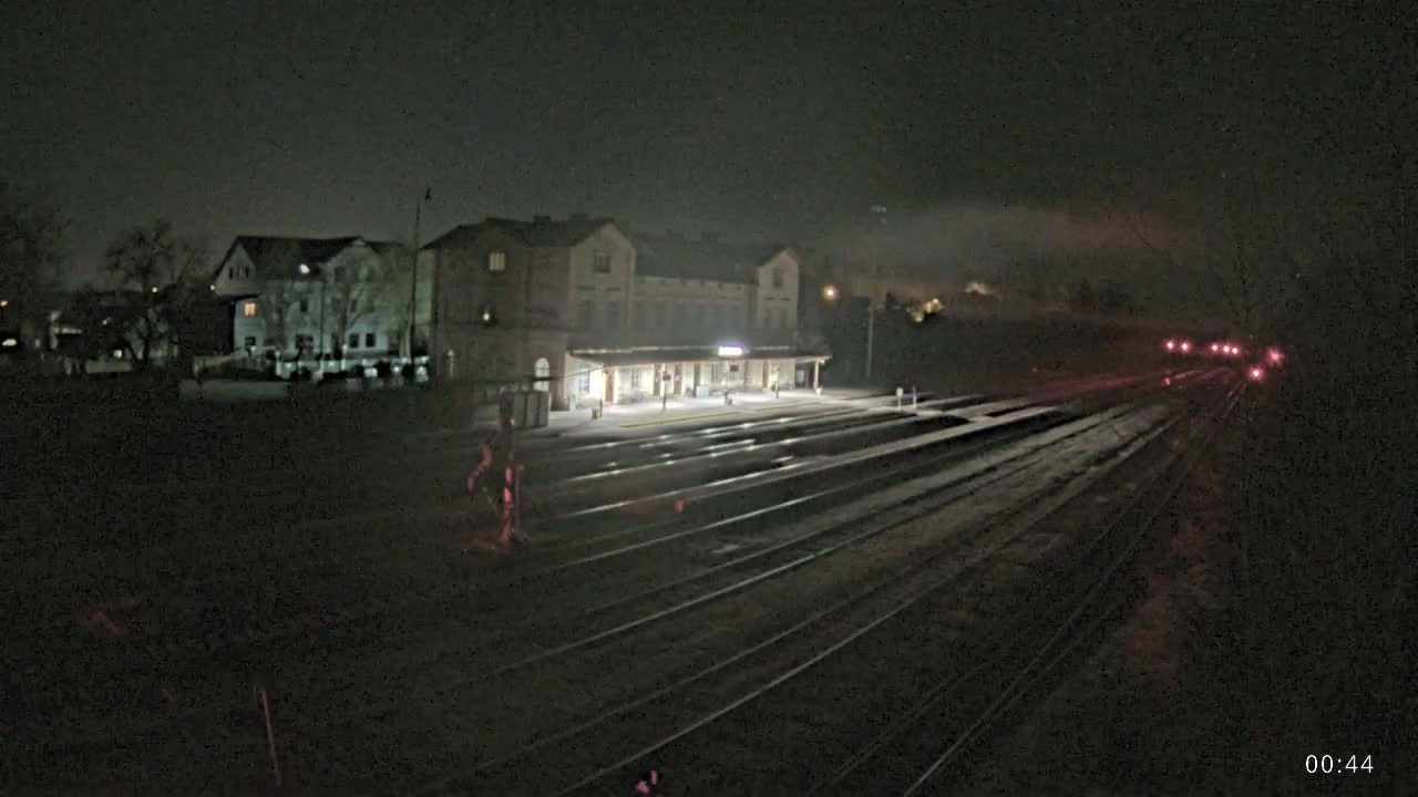 A nighttime view of a train station with several tracks extending into the distance, under a foggy sky.