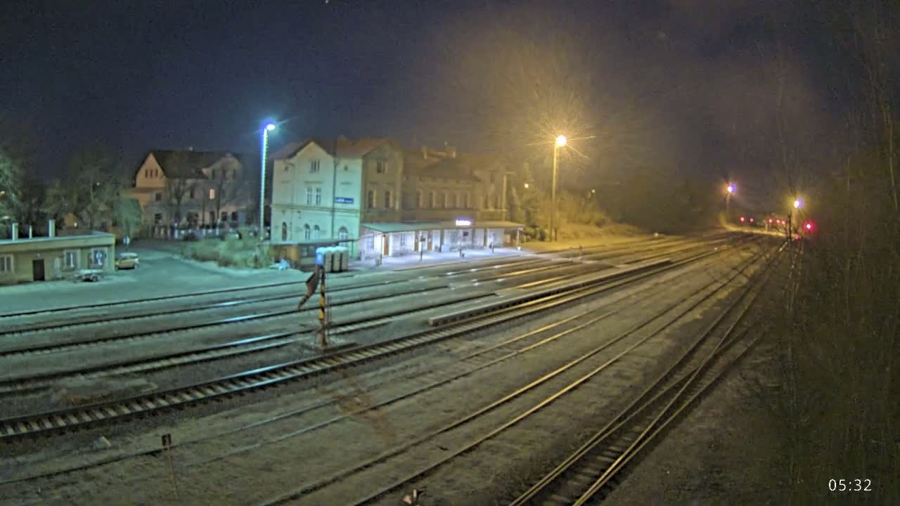 A nighttime view of a train station with multiple tracks extending into the distance under slightly hazy, illuminated conditions.