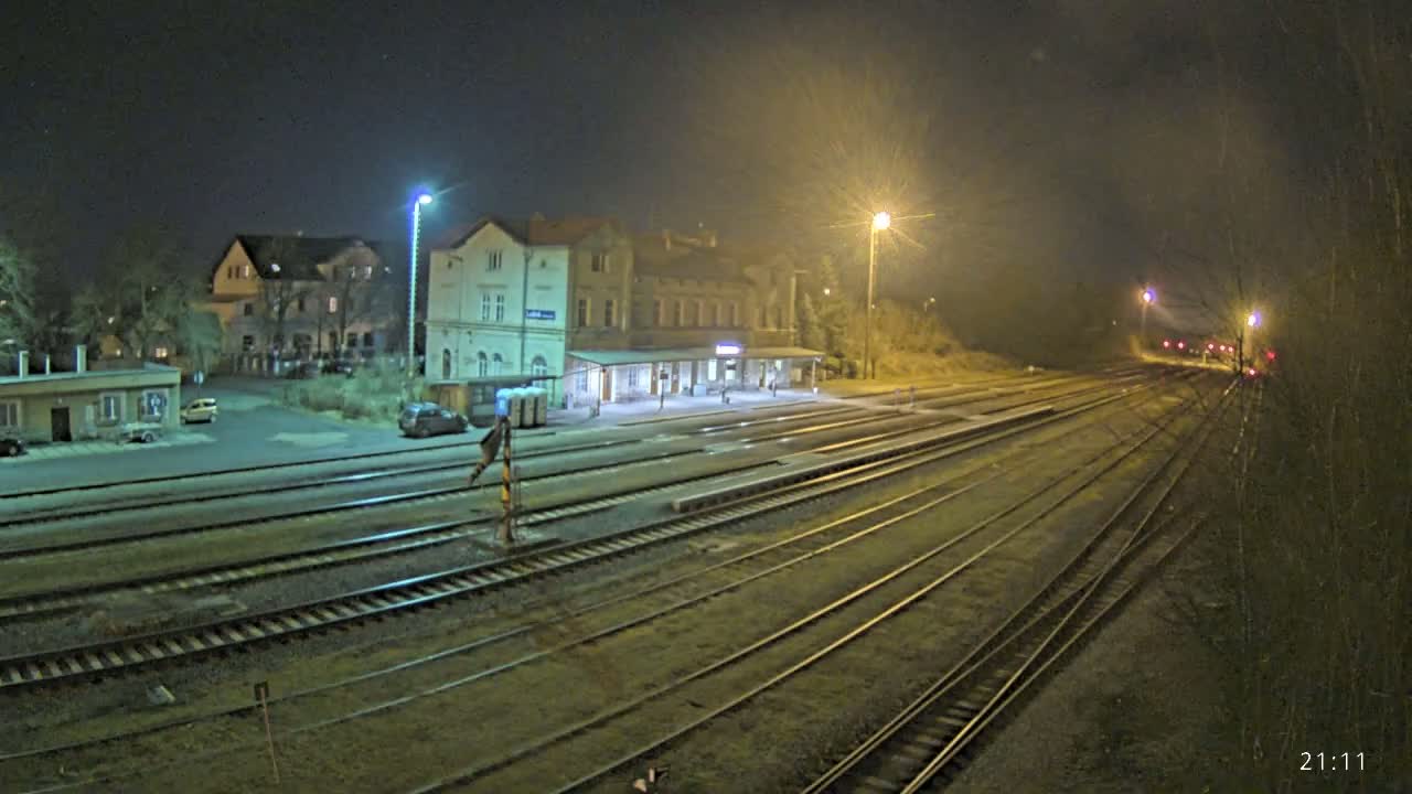 A nighttime view of a train station with several tracks extending into the distance under hazy, well-lit conditions.