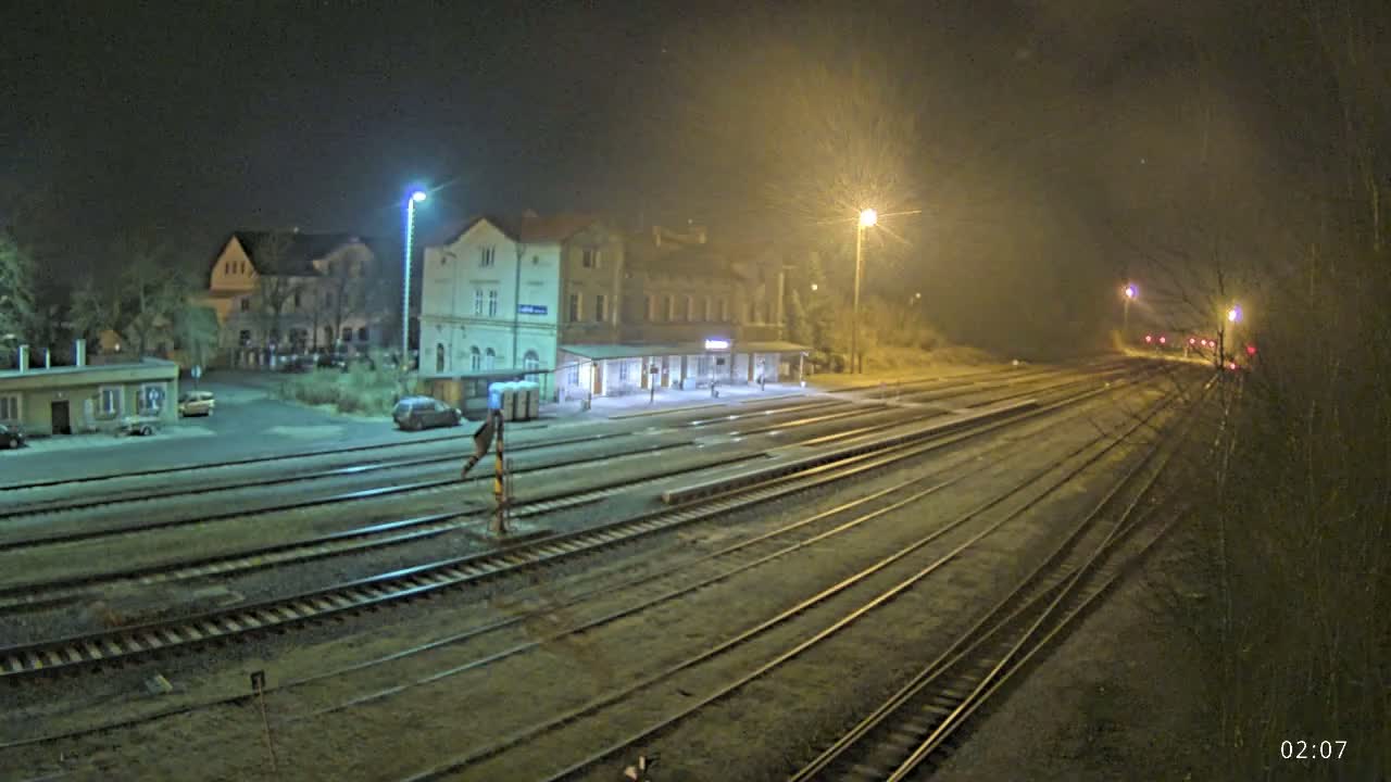 A nighttime view of a train station with several tracks extending into the distance under hazy or foggy conditions.