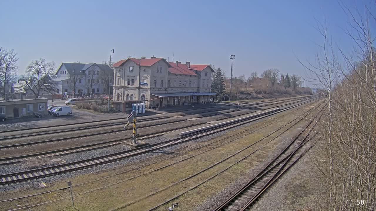 A long view of a train station building and multiple train tracks under a clear, sunny sky.