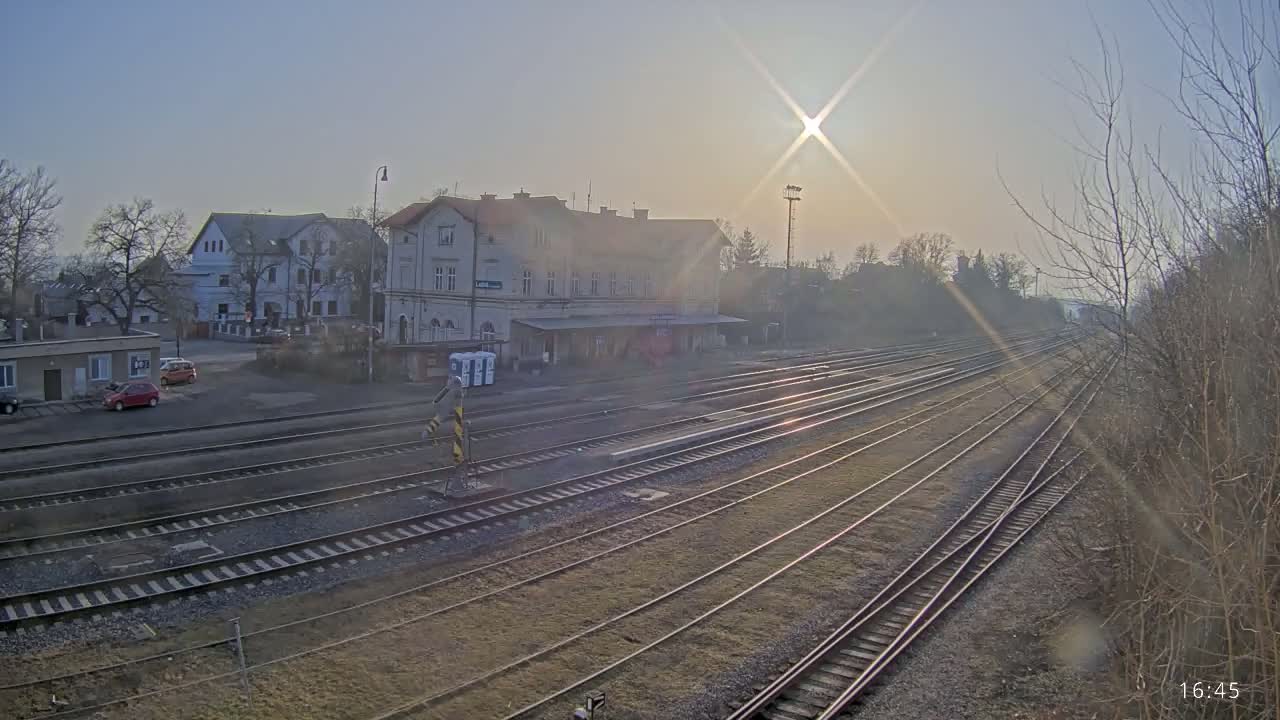 A train station with a long expanse of train tracks extending into the hazy distance under a bright, sunny sky.