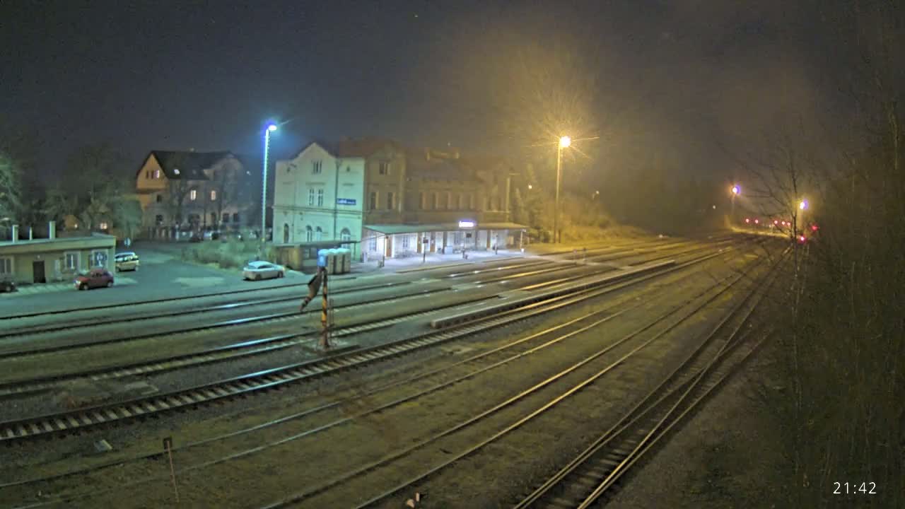 A nighttime view of a train station with several tracks extending into the distance under hazy, dimly lit conditions.