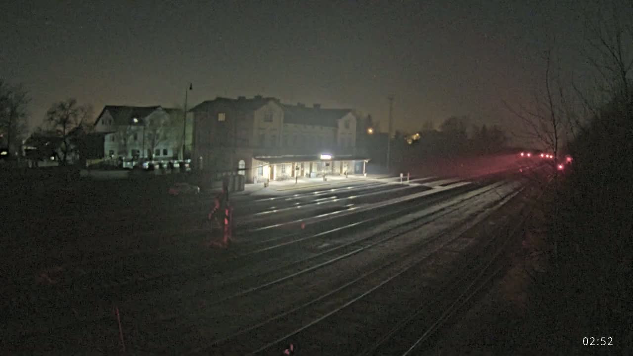 A dimly lit train station at night, under a dark, possibly snowy, sky, with a train approaching in the distance.