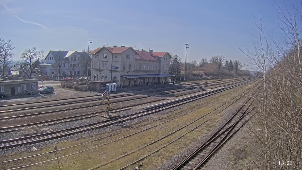 A long view of a train station with a large building and multiple train tracks under a clear, sunny sky.
