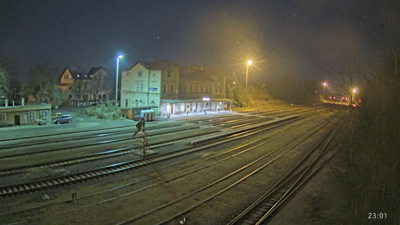 A nighttime view of a train station with several tracks extending into the distance under hazy, dimly lit conditions.