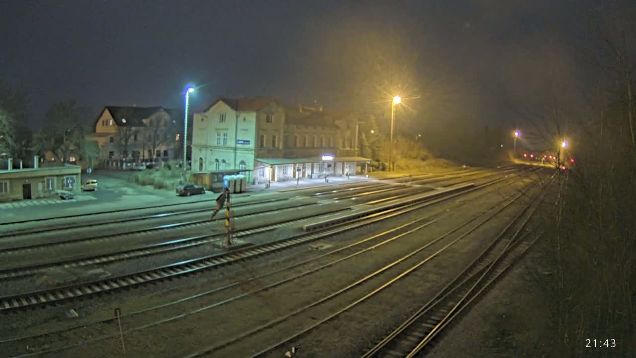 At night, under hazy conditions, a train station with a long platform and multiple train tracks extends into the distance.