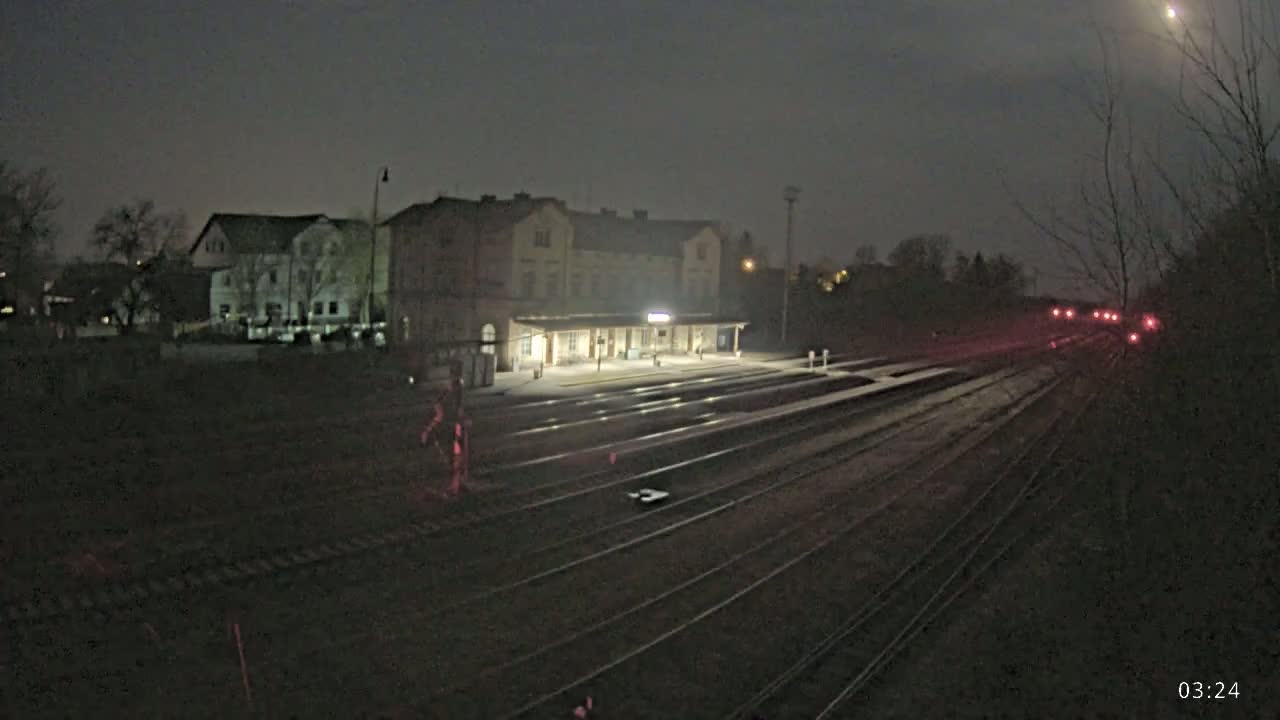 A nighttime view of a train station with multiple tracks extending into the distance, under a dark, moonlit sky.