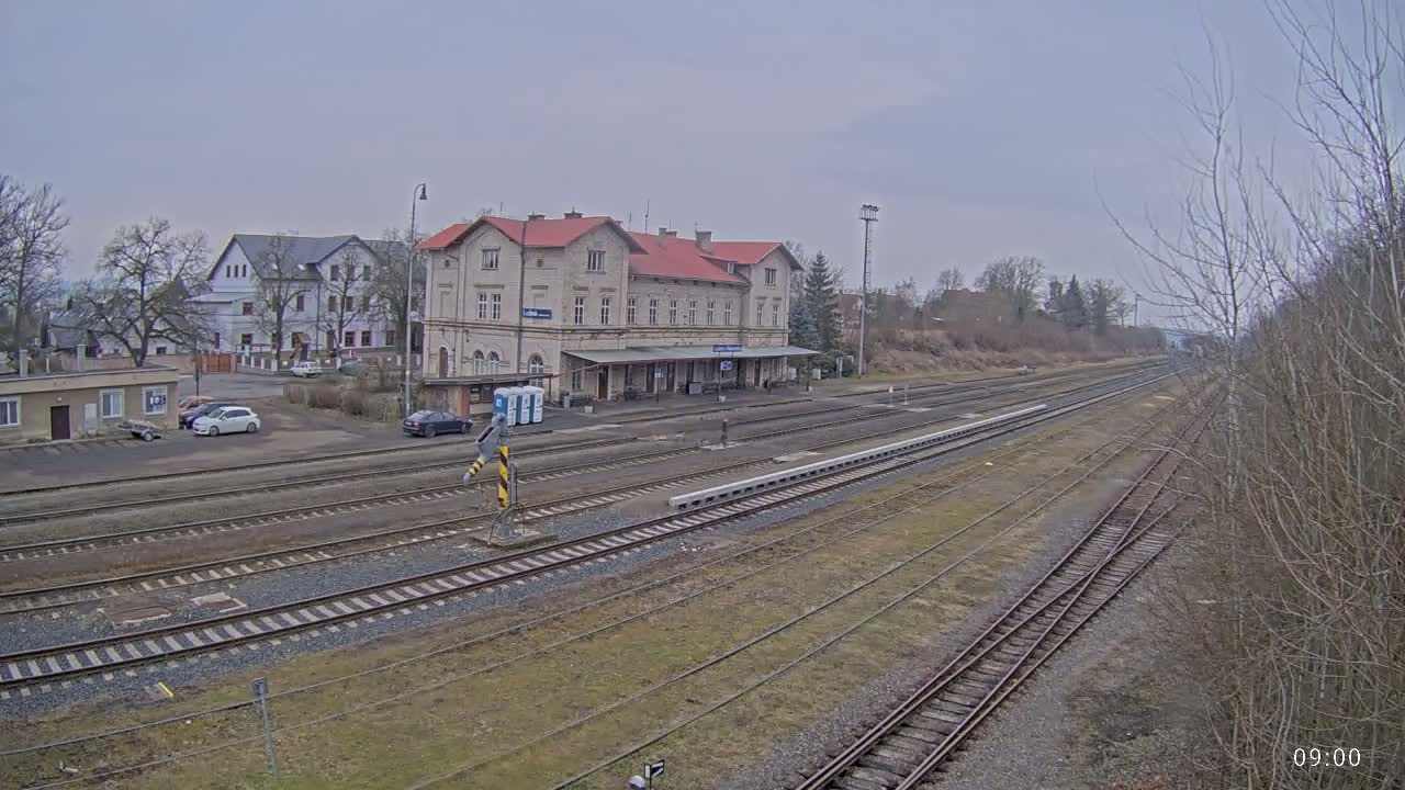 A long view of a train station with a large building and several train tracks under an overcast sky.