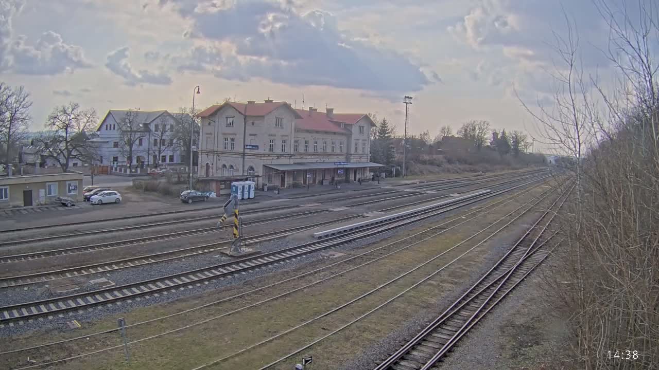 A long view of a train station with a large building and multiple train tracks under a partly cloudy sky.