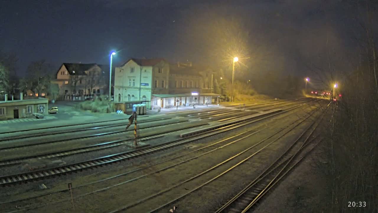 A nighttime view of a train station with multiple tracks extending into the distance under hazy, dimly lit conditions.
