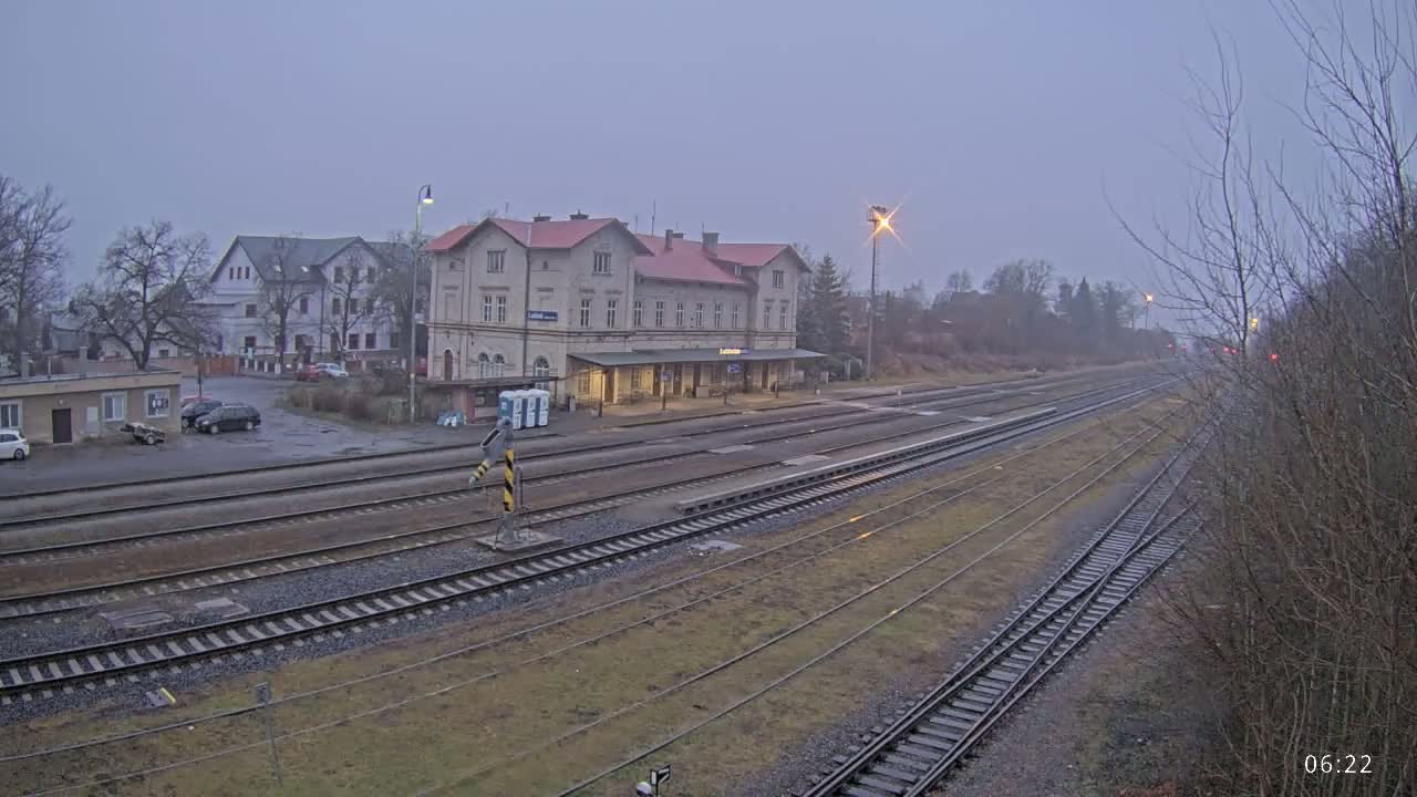 A train station building and several train tracks are visible under an overcast sky.