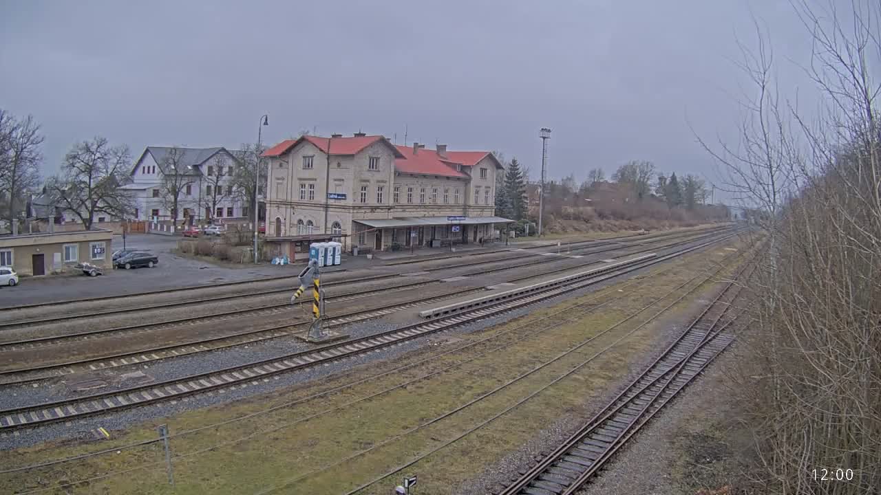 A long view of a train station on an overcast day shows multiple train tracks extending into the distance, with a large light-colored building at the center.