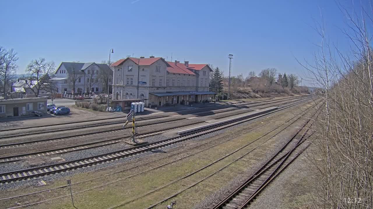 A train station with a long platform and multiple train tracks stretches into the distance under a clear blue sky.