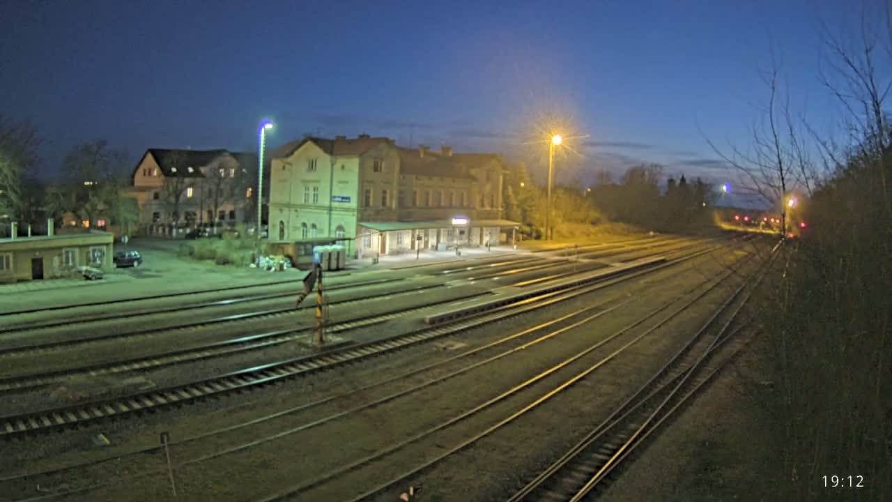Under a twilight sky, a train station with a long building and multiple tracks extends into the distance.