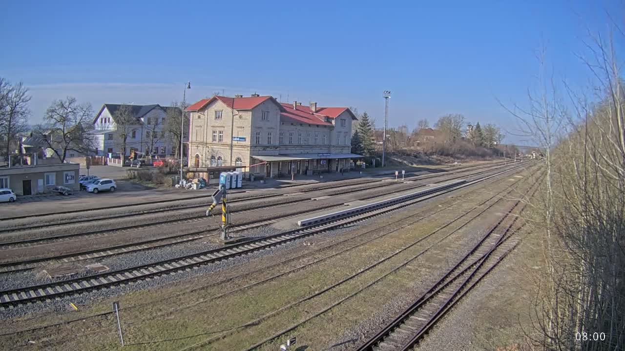 A long view of a train station with a large building and several train tracks under a clear blue sky.